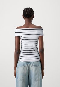 Λευκή μπλούζα με ρίγες σε μαύρ�ο χρώμα, off-the-shoulder και ριγέ. Διαθέτει εφαρμοστό σχέδιο και λεία υφή. Συνδυάζεται με ανοιχτό μπλε τζιν.