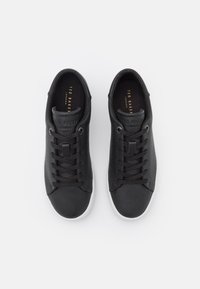 Ett par svarta läder sneakers från Ted Baker med snörning och vita sulor, visade ovanifrån på en vit bakgrund.