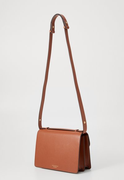 Bolso de hombro de cuero marrón con una correa larga, que presenta un diseño elegante y un logo dorado en la parte frontal, sobre un fondo blanco.