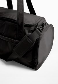 Sort duffelbag med et blødt, tekstureret stof. Har en lynlåslukning, justerbar skulderrem og dobbelte håndtag, designet til alsidighed.