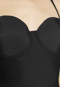 Czarny bandeau wykonany z gładkiego materiału z usztywnianą miseczką, wyposażony w formowane miseczki i cienkie ramiączka, zapewniający pewne dopasowanie.