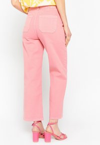 Pantalones rosas de cintura alta con corte recto, dos bolsillos traseros y una textura suave. Combinados con tacones rosas de punta abierta.