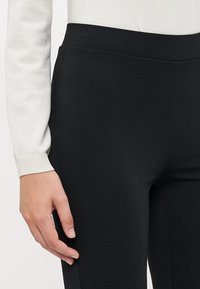 Zwarte leggings van een gladde, rekbare stof met een hoge tailleband, gecombineerd met een witte lange mouw top met ribgebreide manchetten.