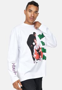 Camisa blanca de manga larga hecha de algodón con un audaz estampado gráfico y texto en verde, con acentos morados en la manga. Corte informal.