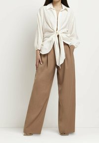 Cream linen button-up shirt tied at the waist, paired with wide-leg brown trousers. Soft texture with a relaxed silhouette.