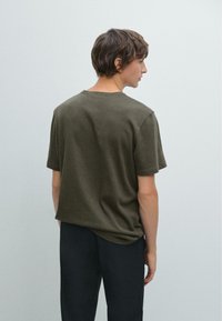 Short-sleeve, relaxed-fit olive green t-shirt, soft texture, round neckline, back view, paired with dark trousers, minimal design.