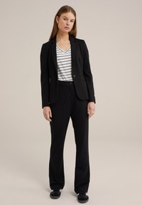 Černý sako přes bílo-černý pruhovaný top, doplněné černými kalhotami a teniskami. Celý vzhled má tailored střih a hladkou texturu.