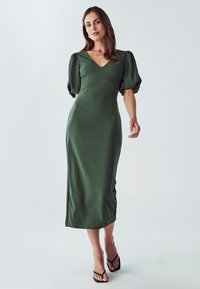 Grünes Midikleid mit V-Ausschnitt, Puffärmeln und figurbetonter Silhouette. Hergestellt aus glattem Stoff, mit Seitenschlitzen und minimalistischer Gestaltung.