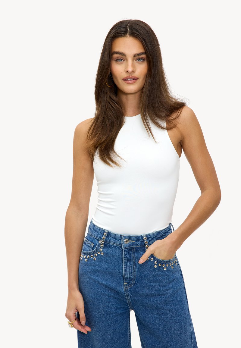 Body blanc sans manches associé à un jean en denim bleu taille haute avec des accents cloutés argentés le long des poches avant.