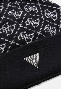 Czarna dzianinowa czapka beanie z powtarzającym się białym wzorem i trójkątną srebrną naszywką z logo. Miękka tekstura i dopasowany krój.