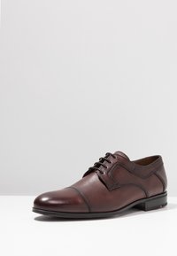 Chaussure habillée en cuir marron avec un bout arrondi et un design à lacets. Présente une finition lisse et des détails de couture subtils. Comprend un petit talon.