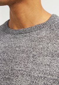 Szary sweter o fakturowanej powierzchni z prążkowanym okrągłym dekoltem, posiadający subtelny wzór w drobne cętki. Miękka dzianina, ściśle dopasowana wokół szyi.