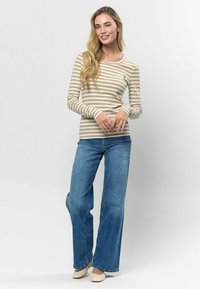 Svītrains garām piedurknēm tops bēšā un krēmkrāsā, apvienots ar gaiši ziliem platām kājām džinsiem. Modelis valkā austas espadrillēs, brīva forma, ribota tekstūra.