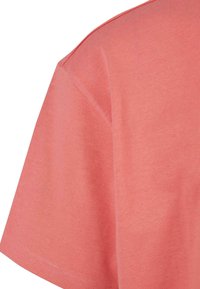 Korall színű pamut T-shirt, sima, bordázott textúrával, laza szabással és rövid ujjakkal. A nyakkivágás kerek, díszítések nélkül.