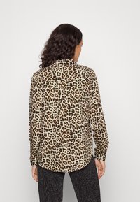 Chemise à manches longues en tissu doux avec un motif léopard, dotée d'un col et d'un ourlet arrondi. La vue arrière révèle le motif détaillé et les poignets à bouton.