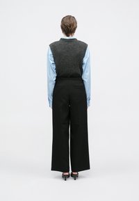 Pelēks adīts veste pāri gaiši zilai svītrainai pogai, kopā ar melnām augsta vidukļa platajām biksēm un melnām kurpēm ar papēžiem.