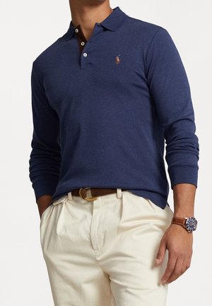 Granatowy polo z długim rękawem, klasycznym kołnierzykiem, zapięciem na trzy guziki i haftowanym logo. Połączony z jasnymi spodniami w kolorze khaki.