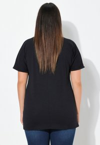 Czarna koszulka krótki rękaw o luźnym kroju, wykonana z miękkiego materiału, z zaokrąglonym hemem i prostym wzorem na plecach.