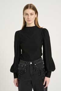 Black long-sleeve top with a high neck and puffed shoulders; paired with high-waisted black jeans featuring hanging beaded accents.