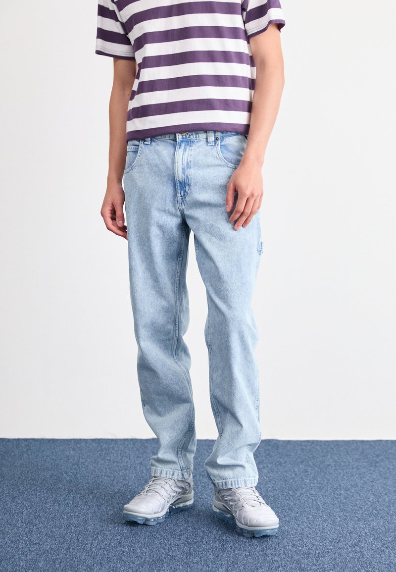 Svetlo modri denim hlače s sproščenim krojem, z zasnovo petih žepov in rahlimi poškodbami. Upoštevane s purpurno in belo črtasto majico.