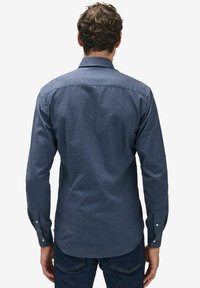 Jeansskjorta i mörkblått, med långa ärmar, knäppning vid kragen, rundad nederkant och knäppning vid ärmsluten. Slät textur, avslappnad passform och minimal detaljering.