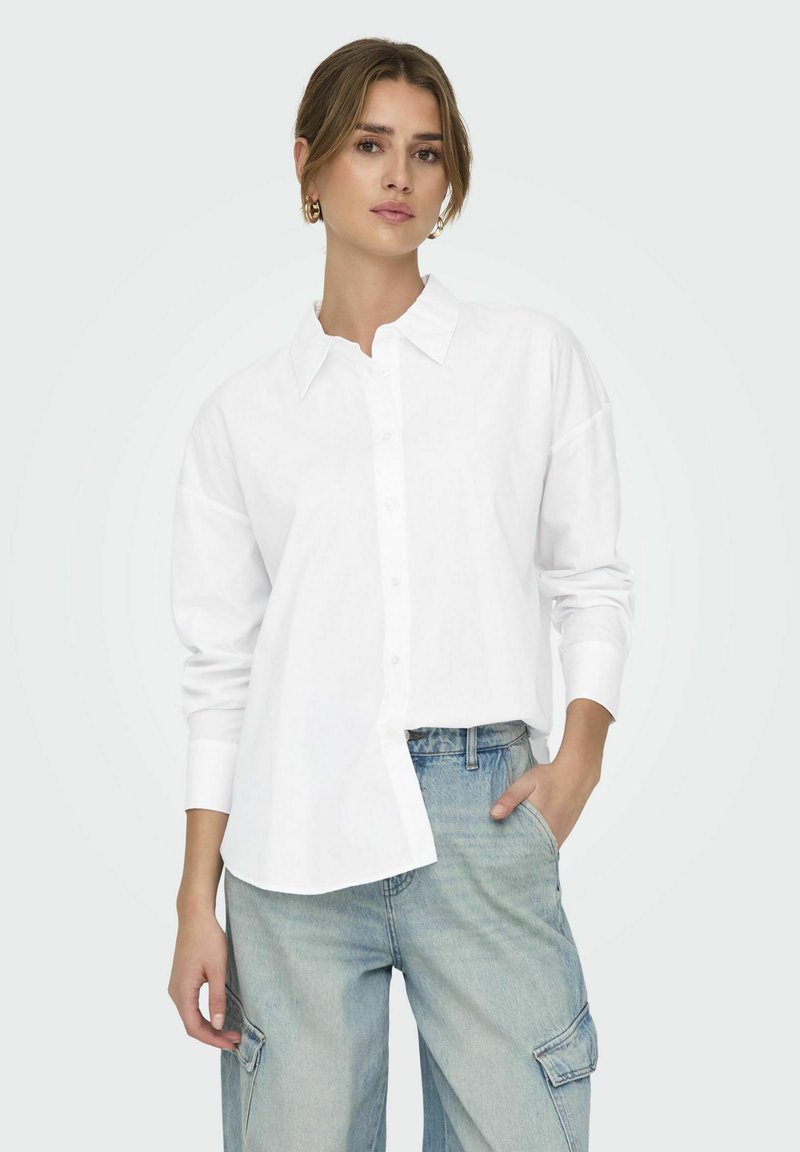 Camicia bianca con colletto e maniche lunghe, caratterizzata da una vestibilità rilassata e un orlo dritto, abbinata a jeans in denim blu chiaro.