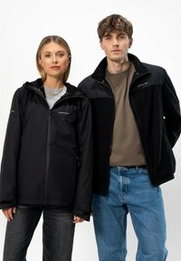 Černé bundy se zapínáním na zip, s kapucí a kapsami. Jedna má měkkou texturu; druhá má hladký povrch. Obě jsou doplněny o pohodlné džíny.