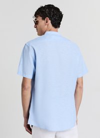 Chemise bleu clair à manches courtes avec une coupe décontractée, présentant une texture subtile et un ourlet droit. Vue de dos, sans motifs ni accents visibles.