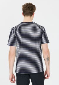 Námořnické a bílé pruhované tričko s krátkým rukávem, kulatým výstřihem a rovný střih, s viditelným tetováním na předloktí.