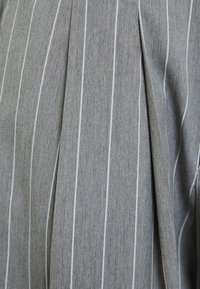 Tissu gris avec de fines rayures verticales blanches et un détail de pliage prononcé, montrant la texture et le motif d'un vêtement ajusté.