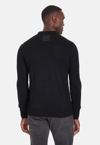Maglione nero lavorato a maglia con maniche lunghe, polsini e orlo a coste, con una toppa quadrata con logo sul retro del collo.
