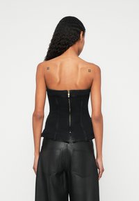 Zwarte denim korset-top met een gestructureerd ontwerp, voorzien van een rits aan de achterkant en een peplum-rand, gecombineerd met hooggesneden zwarte leren broek.