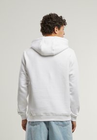 Vit hoodie med dragsko i huvan och ribbade manschetter. Tyget verkar mjukt och mysigt, med en enkel, odekorerad design.