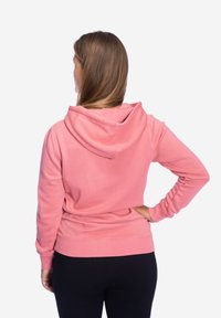 Rosa Kapuzenpullover mit lockerer Passform, gerippten Bündchen und Saum, weicher Textur und einem Kordelzug an der Kapuze, von hinten betrachtet.