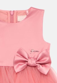 Ροζ σατέν φόρεμα με τούλινη φούστα, μεγάλη κορδέλα στη μέση και φερμουάρ στην πλάτη. Περιλαμβάνει μεταλ λικό λογότυπο εμπορικού σήματος.