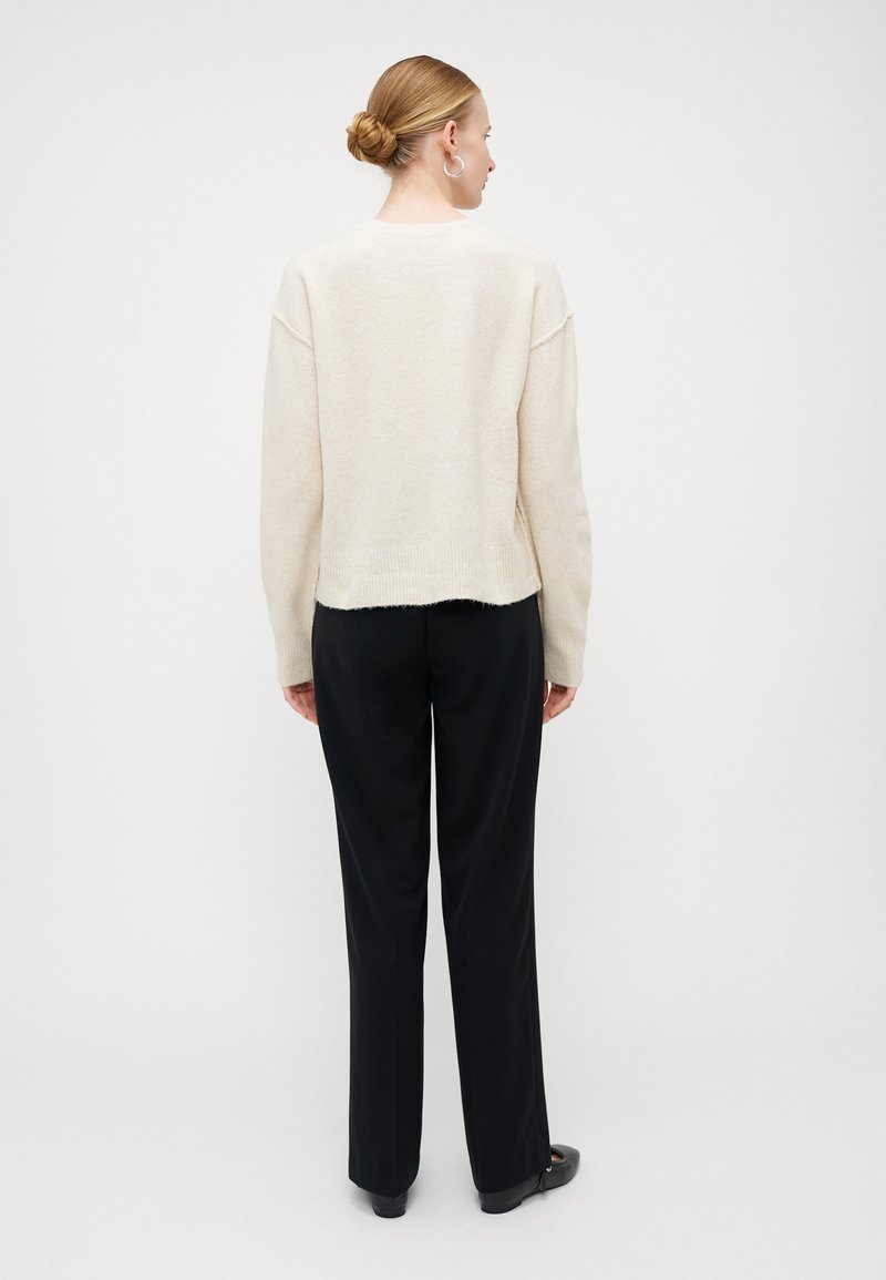 Pull crème clair à coupe décontractée, avec épaules tombées et ourlet côtelé, associé à un pantalon noir ample et des chaussures plates.