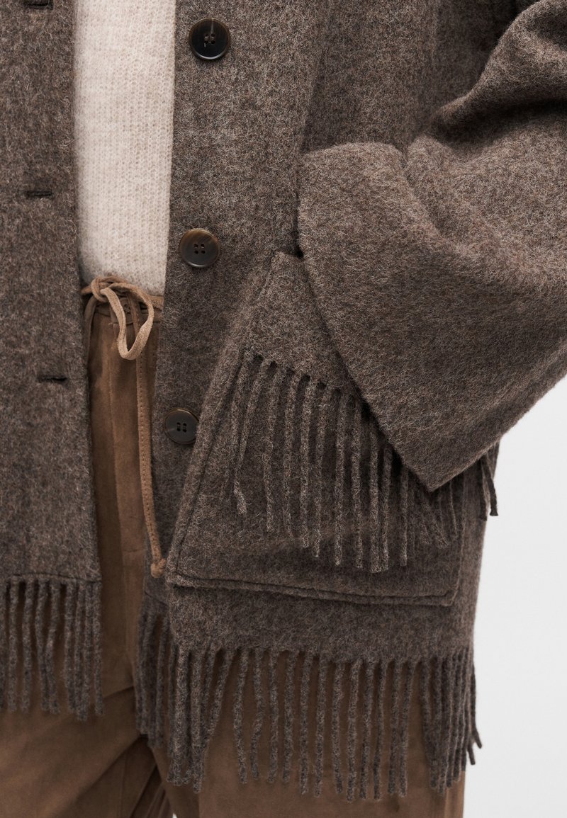 Brun frynset cardigan lavet af struktureret uld, med sorte knapper, en løs pasform og et ekstra blødt lag under.