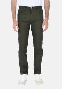 Pantaloni in misto cotone verde con vestibilità slim, dotati di tasche anteriori, chiusura con bottone e cuciture a contrasto, abbinati a sneaker bianche.