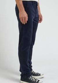 Mörkblå kordfluwelbyxor med slim fit, med sidofickor och en slät textur, bärs med svarta och vita sneakers.