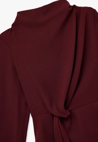 Bordeaux stoffen top met een gedrapeerde halslijn en een strikdetail op de rug. Glad textuur met een matte afwerking, die subtiele plooien in het materiaal laat zien.