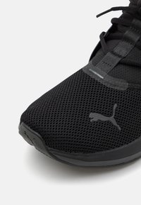 Schwarzer Sportschuh mit einem Obermaterial aus Mesh, das eine strukturierte Oberfläche aufweist, gepolsterten Schaft und ein kleines reflektierendes Detail an der Seite.