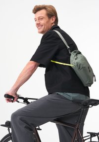 Grüner, packbarer Rucksack mit Zugverschluss und ergonomischem Tragegurt, getragen von einem Mann auf einem Fahrrad. Hellgraue und schwarze Kleidung.