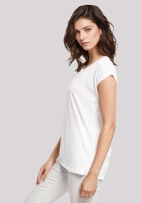 White cotton t-shirt with rolled short sleeves, a rounded neckline, and a relaxed fit, worn with light gray pants.