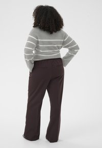 Szary sweter w paski z długimi rękawami, zestawiony z ciemnobrązowymi spodniami o szerokich nogawkach, posiadającymi elastyczny pas i tylne kieszenie.