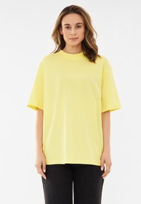 Żółta bawełniana, oversize koszulka z krótkim rękawem, okrągłym dekoltem i gładką teksturą. Noszona z czarnymi dżinsami.