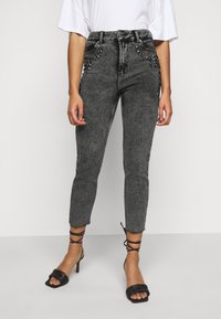 Jeans gris de tiro alto, ajustados, con tejido texturizado, bolsillos delanteros adornados y dobladillos deshilachados. Combinados con sandalias de tacón negras con tiras.