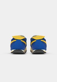 Sinine ja kollane Reebok'i spordijalatsite paar, vaadatuna tagant, rõhutades kontsa ja tallat kontrastset valget tausta vastu.