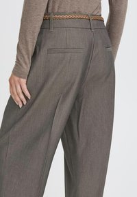 Die Hose aus dunkelgrauem Stoff zeichnet sich durch einen geraden Schnitt, zwei Gesäßtaschen und einen geflochtenen hellbraunen Gürtel aus, was einen maßgeschneiderte Look betont.