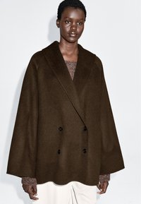 Manteau marron à double boutonnage en mélange de laine, avec un large col et des manches surdimensionnées, orné de boutons noirs et d'un ourlet festonné.