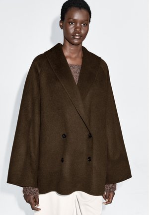 Manteau marron à double boutonnage en mélange de laine, avec un large col et des manches surdimensionnées, orné de boutons noirs et d'un ourlet festonné.